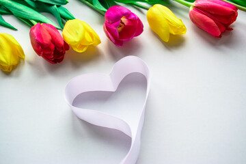 Colorfull fresh tulips flowers with ribbon heart on white background. Greeting card. Flat lay. Copy space.