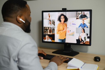 Training, webinar online. A young African guy is watching on the screen with a group of diverse people on it. Multiracial team have online meeting, virtual conference