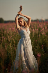 Romantic blonde woman running in a wonderful flower field. Warm sunset colors. Blue dress. Soft colors.