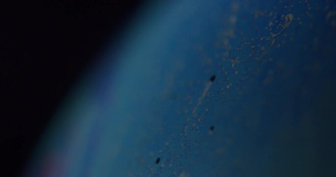 Macro shot of a small section of a sphere. Current visible in the blurry background, dark studio environment. Small details visible in the foreground. Dark spots on the sphere.