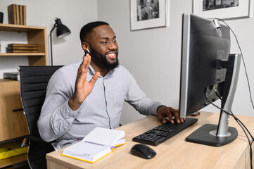 A positive multiracial coach, mentor conducts online webinar, he is waving hand into webcam. An...