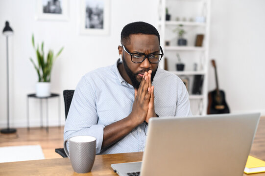 An intelligent African-American student in glasses work at laptop sitting on the chair at home, concentrated and serious working and studying online, focused on completing an assignment