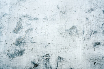 White peeling paint on a concrete wall with brownish black patches emerging from underneath. Close up.