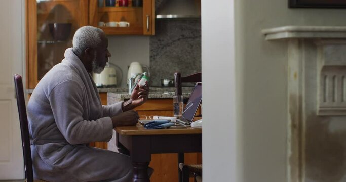 African american senior man holding empty medication while having a video call on laptop at home