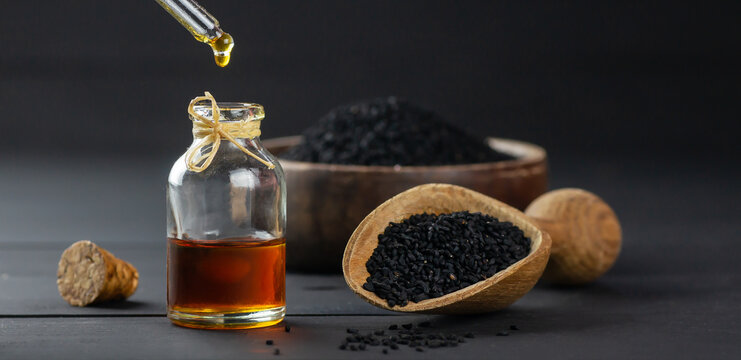 Glass bottle of black cumin seed essential oil , Nigella Sativa in scoop on black wooden background, oil dripping
