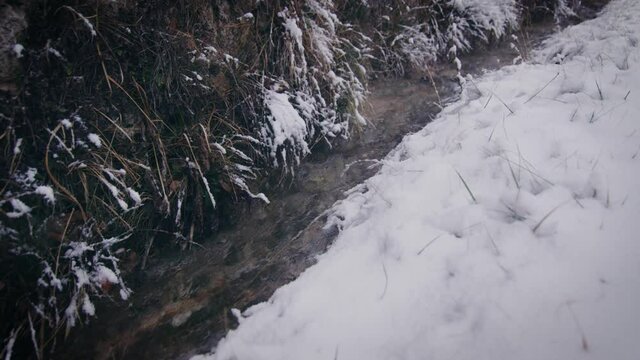Winter scenery trickling brook surrounded by snowy banks. Close up