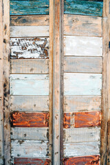 Colored wooden plank tile doors with peeling paint. In vertical rows bounded with longer planks on sides. Painted and naked ones are interchanging.