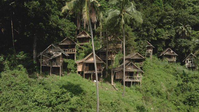 Pan up shot of ramshackle bamboo backpacker huts on a hill in the jungle in Thailand