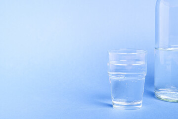 Glass with water near to bottle on blue background