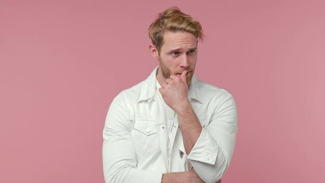 Puzzled pensive confused bearded young man 20s years old in white casual clothes isolated on pastel pink color background studio. People lifestyle concept. Looking aside up put hand prop up on chin
