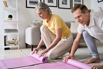 Fototapeta premium Sporty fit middle aged old couple hands rolling or unrolling yoga pilates mat at home. Seniors fitness exercises, elder health and body care training, mature people active lifestyle concept, close up.