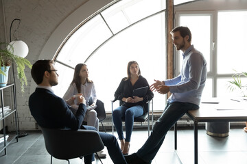 Confident businessman leading briefing, training diverse employees at meeting, colleagues sitting...
