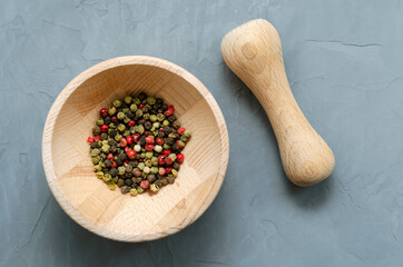 Multicolored red green black peppercorns in a wooden mortar with a pestle on a gray concrete background close-up with a place for text. seasoning. ingredients.