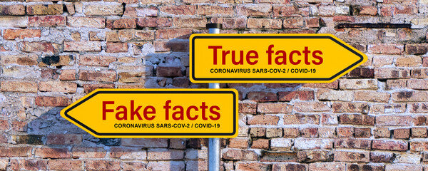 two street signs with message TRUE FACTS and FAKE FACTS regarding the coronavirus SARS-COV-2, COVID-19 in front of a brick wall