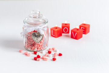 Valentine day background. Vintage glass jar with a white flying jar and a heart with multi-colored candies in the form of hearts. Red candles with the inscription "Love"
