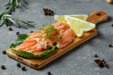 Pieces of fried salmon with dill and lemon wedges on a wooden board