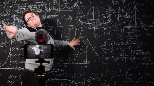 A man is dancing near blackboard full of formulas and graphics in front of mobile camera. Mathematics teacher takes a break during an online lesson. Funny professor is recreating at distance education