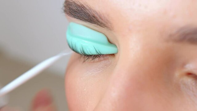 Face of a young girl in a modern eyelash lamination procedure in a professional beauty salon. Master apply black dye paint to the eyelashes during the eyelash curling procedure with a special brush.