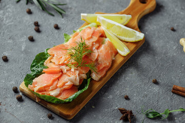 Pieces of fried salmon with dill and lemon wedges on a wooden board