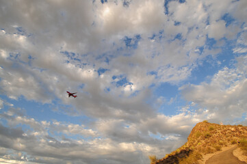 Commercial airliner flying through a cloud-streaked sky above desert hillside terrain, illustrating regional air traffic, aviation routes, and Southwestern geographic overflight patterns
