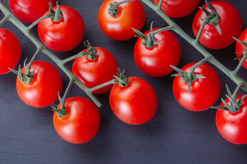 Ripe cherry tomatoes on a branch on a wooden dark background. Top view, copy space.