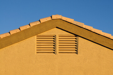 A close-up, horizontal exterior view of the top of a single-family home wall features an attic vent and a ceramic tile roof.