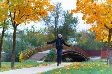 a girl walks along the path and enjoys autumn, maples with yellow leaves and a bridge over the river