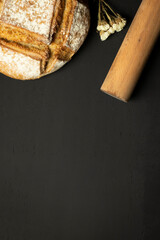food frame with bread, rolling pin and flower on black background. space for text.