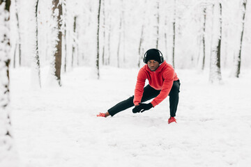 Fototapeta na wymiar Young african american man doing exercise on winter day in forest