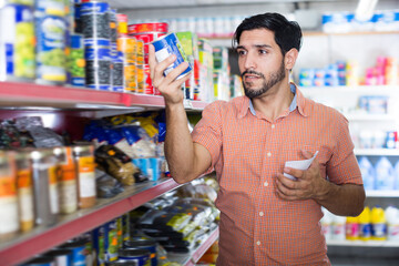 Adult man is choosing conserved peas with help note list in market