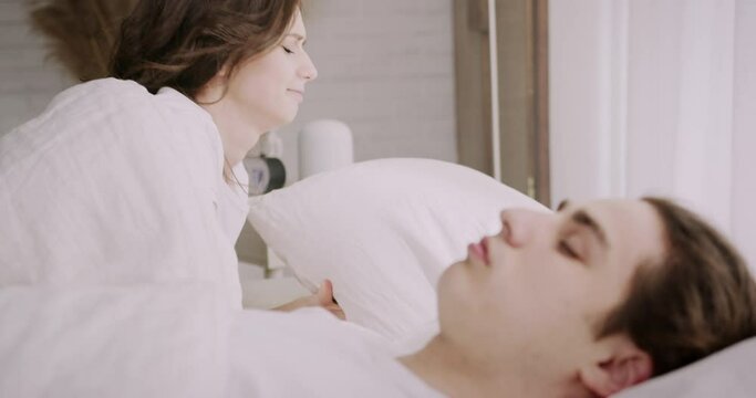 Family couple lying together in bed. Husband snoring loudly, preventing wife from falling asleep. Irritated woman staying awake, covering ears with pillow.