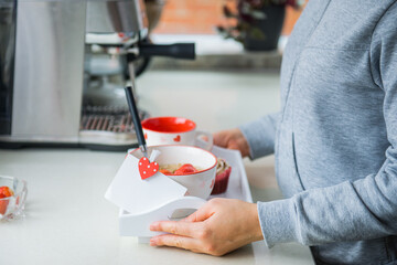 Woman holding a tray with oatmeal porridge bowl with strawberries, a cup of coffee, cupcake, and blank greeting card. Surprise breakfast for lover on Valentines' day. Simple festive healthy food idea.