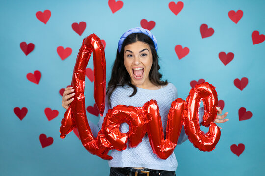 Young beautiful woman over blue background with red hearts holding the word love balloon