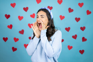 Young beautiful woman over blue background with red hearts shouting and screaming loud to side with hands on mouth