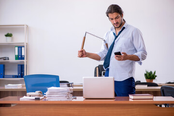 Young male furious employee holding nun-chucks in the office