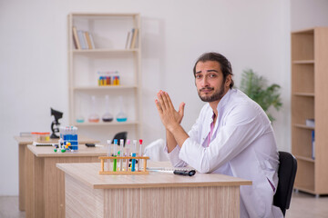 Young male chemist sitting at the desk in the classroom