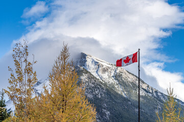 National Flag of Canada with Mount Rundle mountain range in a snowy sunny day. Banff National Park, Canadian Rockies.