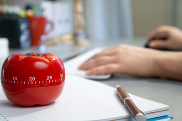 Shallow focus shot of a tomato-shaped timer and notebook on the table