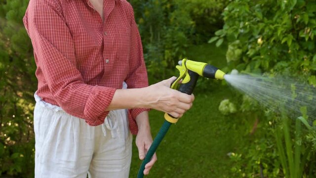 Woman gardener watering plants with hose with sprinkler in sunny backyard. Gardening. Seasonal work in the garden. Close-up picture of hands and spray bottle.