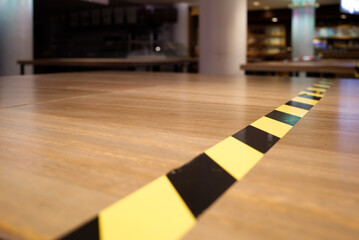 Selective focus view at black and yellow caution tape on wooden tables of closed restaurant during lockdown from epidemic of COVID-19 virus. 