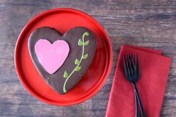 Heart shaped chocolate cake on a red platter and wood background, Valentine’s day treat
