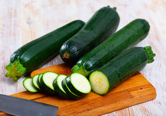 Closeup of fresh zucchini with chopped slices on wooden surface. Vegetarian food concept