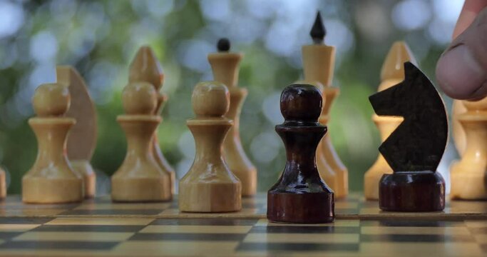 Game of chess. A man's hand puts a chess piece on a chessboard that stands in the garden. Closeup.