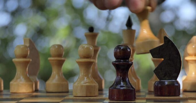 Game of chess. A man's hand puts a chess piece on a chessboard that stands in the garden. Closeup.