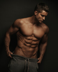 Male fitness model standing on black background with holding his pants