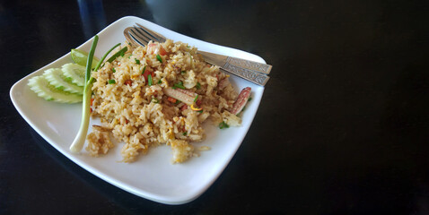 Thai food crab fried rice and cucumber on white plate black background.