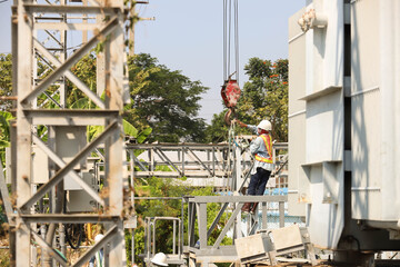 Workers attach a strap to the crane loop to lift the workpiece.