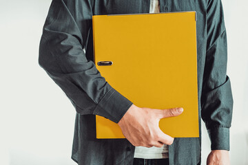 Shoot of man with blue shirt who is standing, holding folder on a white background.