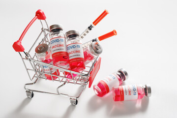 Wire shopping cart with vaccine vials bottles and syringes for vaccination against COVID-19 SARS-CoV-2 coronavirus pandemic on white background, copy space