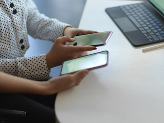 Female hands holding two smartphone on the table in office room